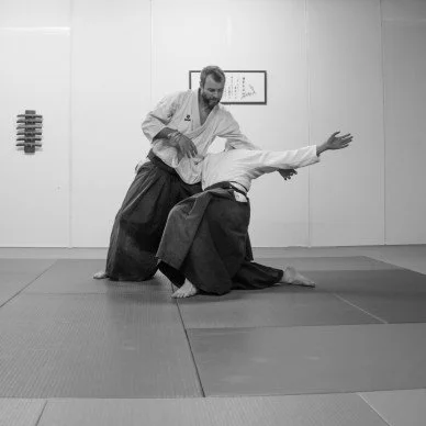 Two martial artists practicing Aikido techniques in a dojo, with one executing a throw on the other.