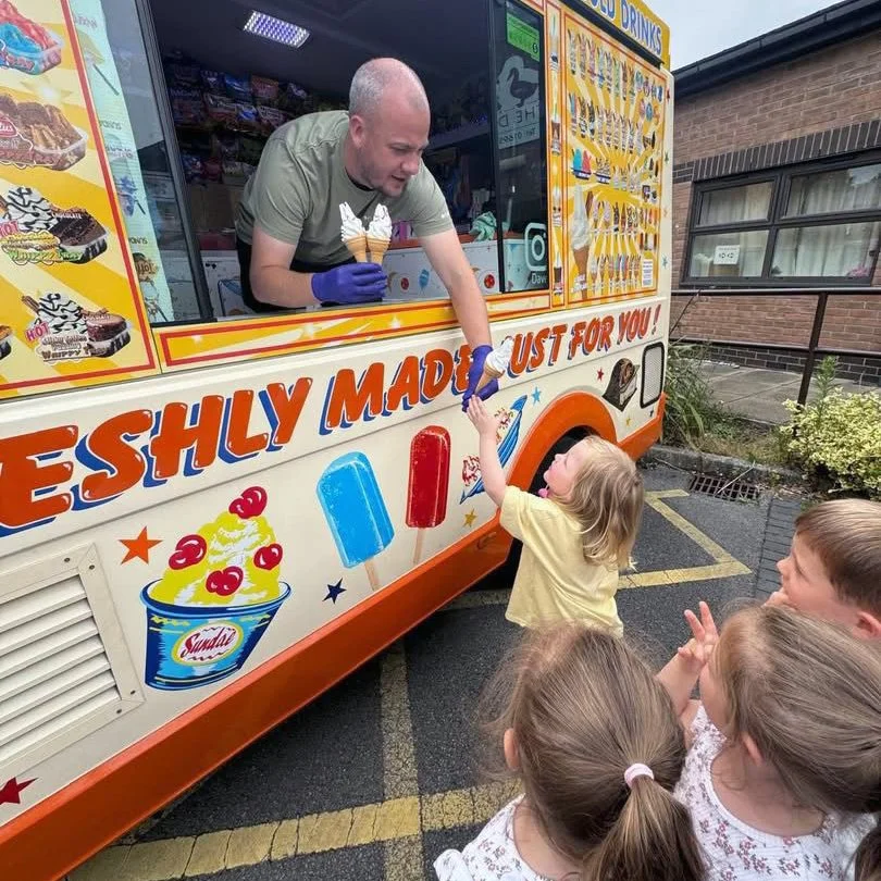 A man working at an ice cream truck with a young girl handing him money, and three other children watching nearby.