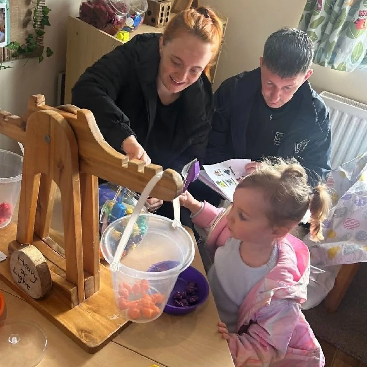 Nursery practitioner supporting a child during a hands-on balancing play activity.