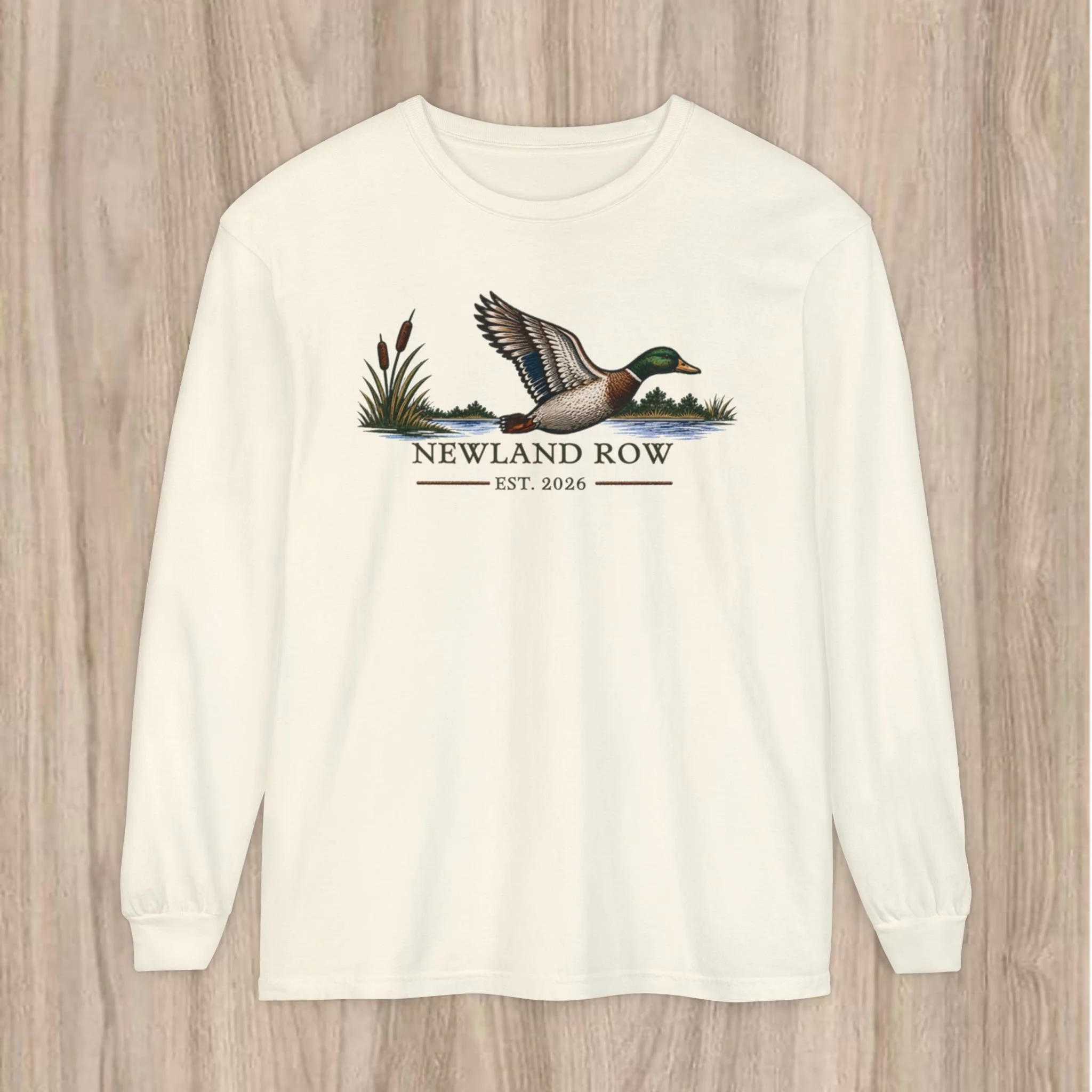 Lightweight, garment-dyed long sleeve with a nature-inspired centerpiece — a flying mallard over marsh reeds, paired with a clean, vintage-style wordmark.