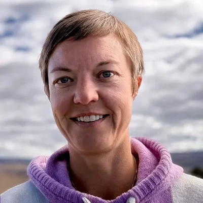 A woman with short hair smiling outdoors with cloudy skies in the background.