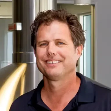 A man with brown hair smiling in an indoor setting.