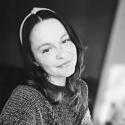 A young woman with dark hair and a headband, smiling gently at the camera, in black and white.