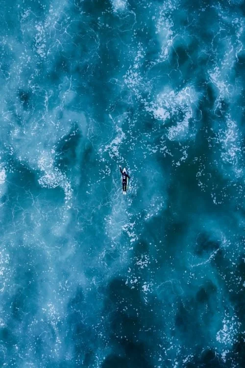 A person kayaking on rough ocean waters seen from above.