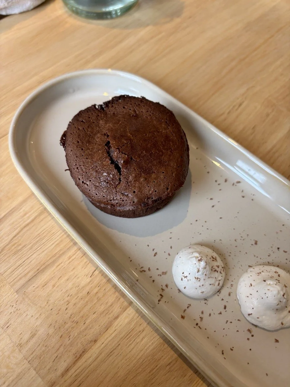 Gâteau au chocolat rond avec deux petites boules de crème ou de mousse, décorées de chocolat râpé, sur une assiette blanche