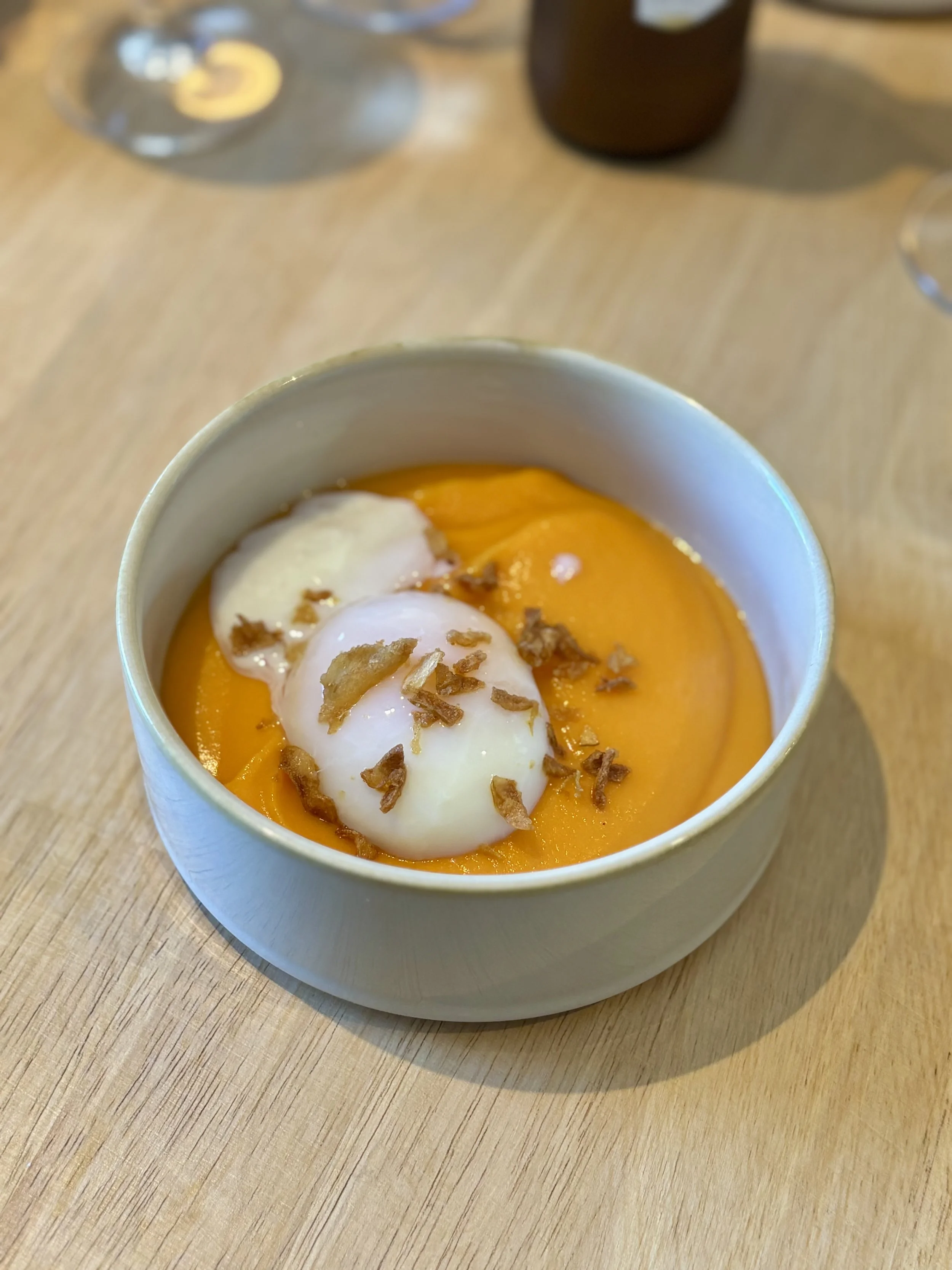 Oeuf poché avec purée de patates douces, garnie de bacon grillé et d'une sauce blanche, dans un bol blanc sur une table en bois.