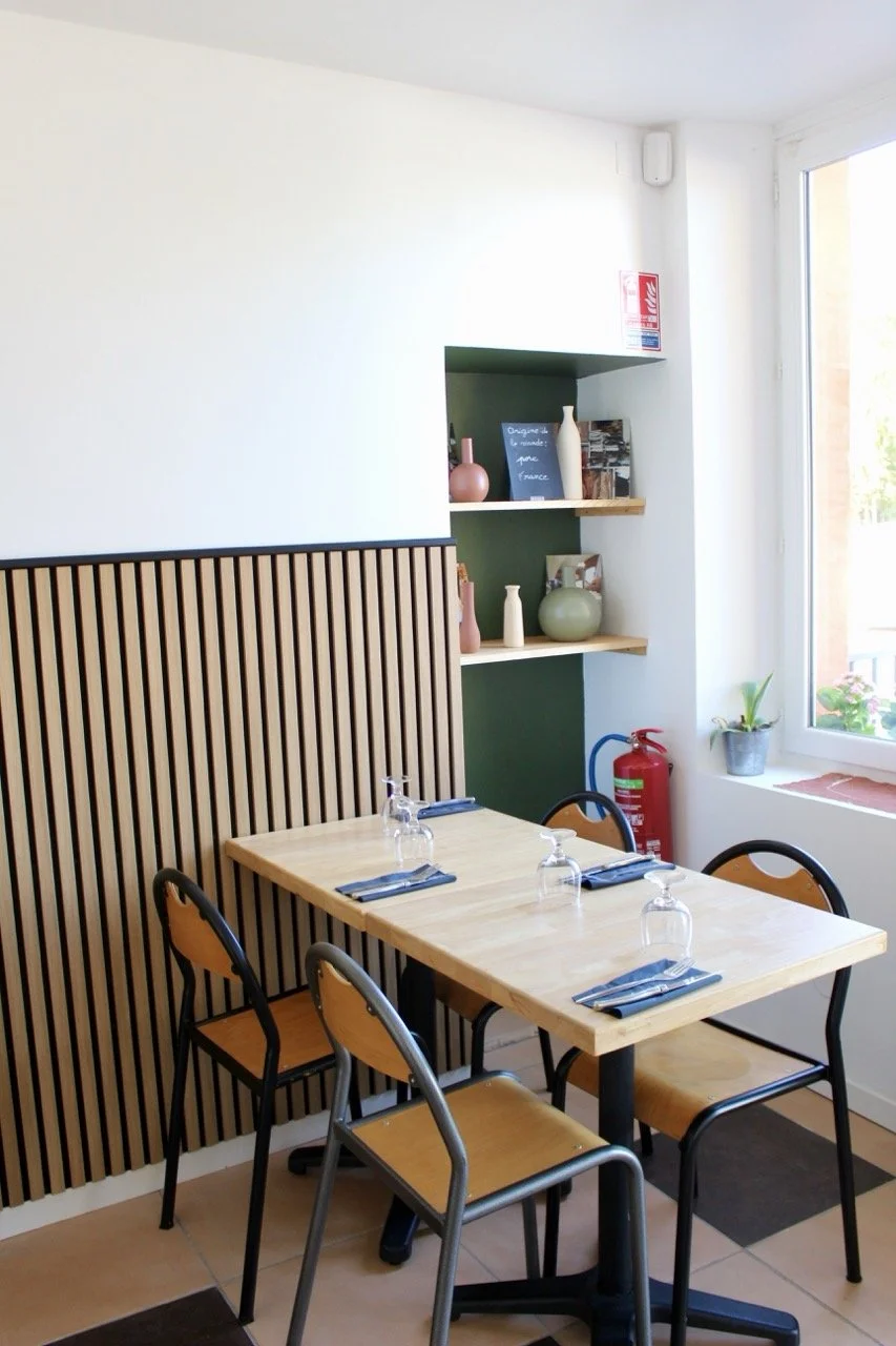 Salle à manger avec une table en bois, quatre chaises, un mur avec une cloison en bois, des étagères avec des décorations, une fenêtre avec plante et abri contre le feu.