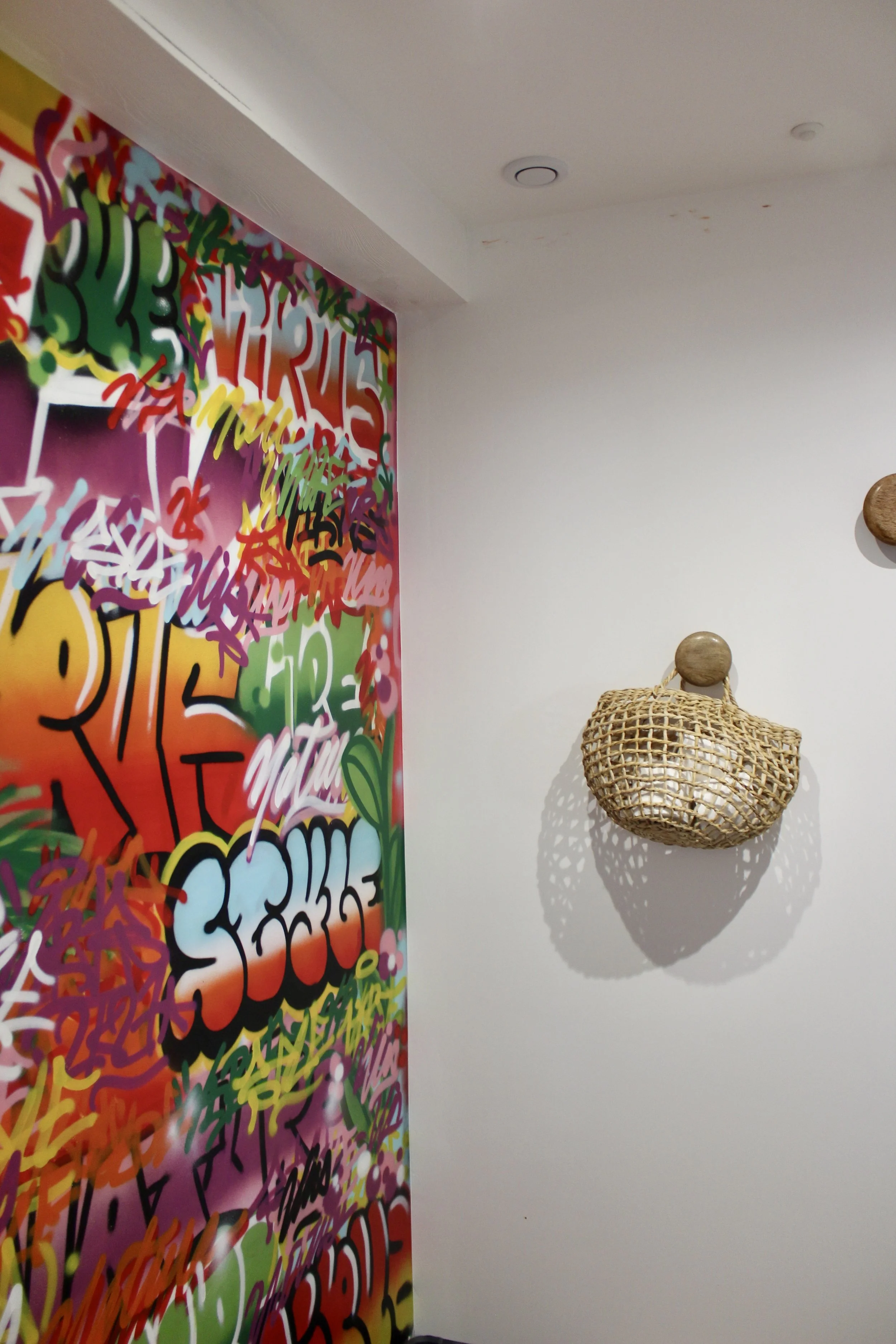 Un mur blanc avec une pièce d'art en rotin suspendue et un mur coloré avec graffiti