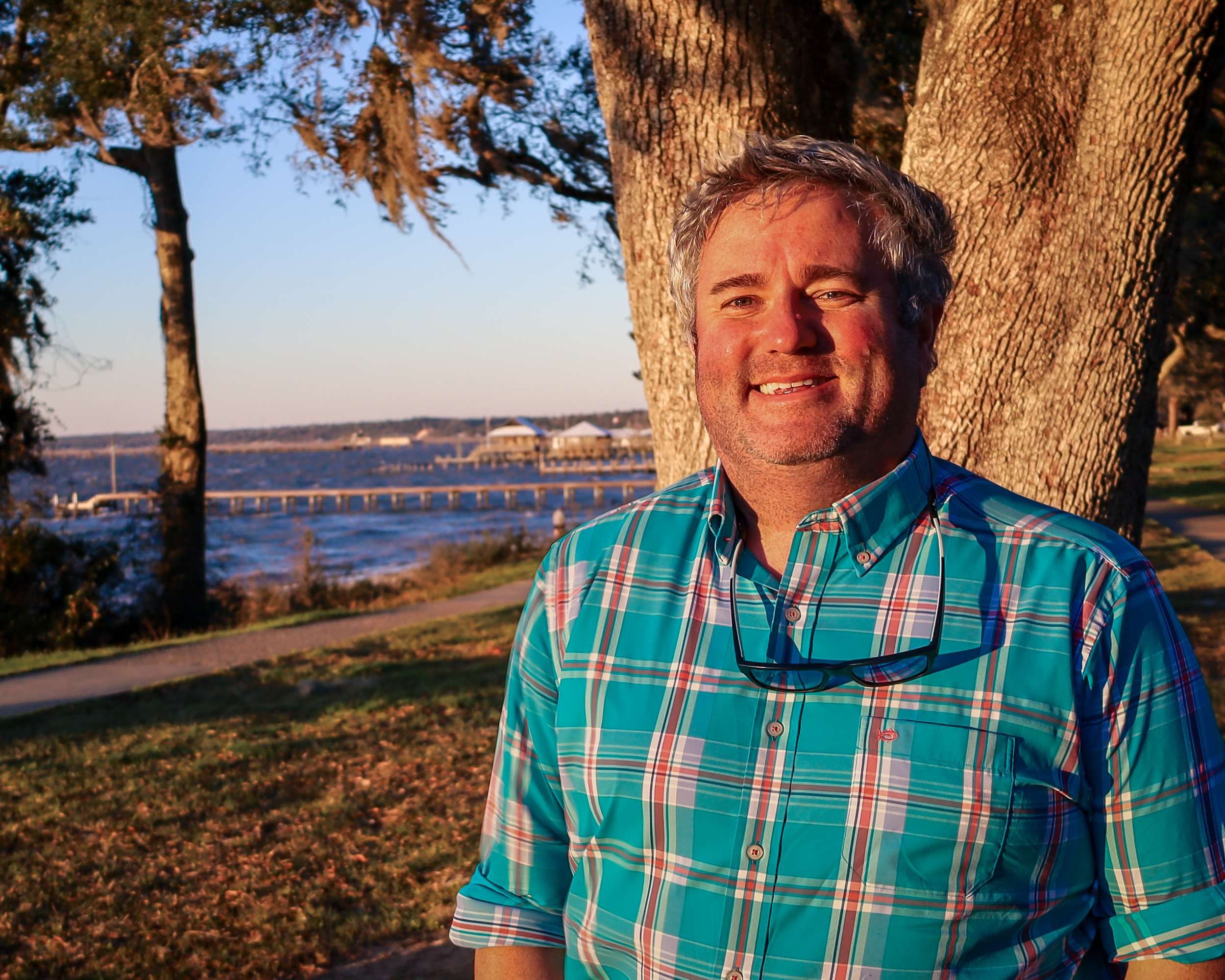 A smiling male therapist (Chandler, AZ) smiling outdoors near a waterfront, professional headshot for counseling services