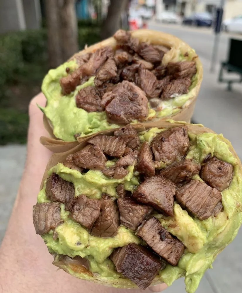Close-up of a hand holding two avocado toast wraps filled with chopped beef