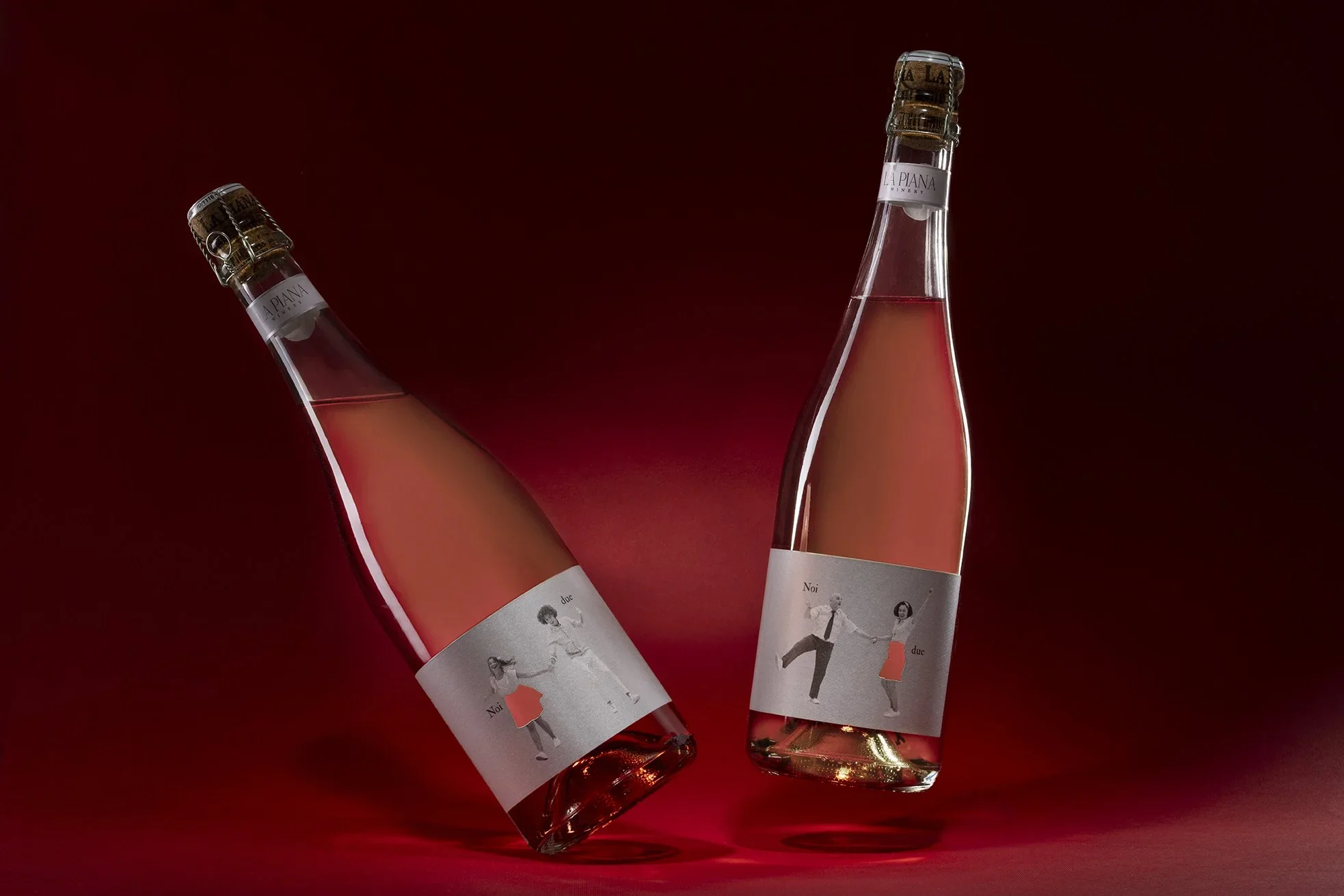 Two bottles of rosé wine with illustrated labels featuring people dancing, set against a red gradient background.