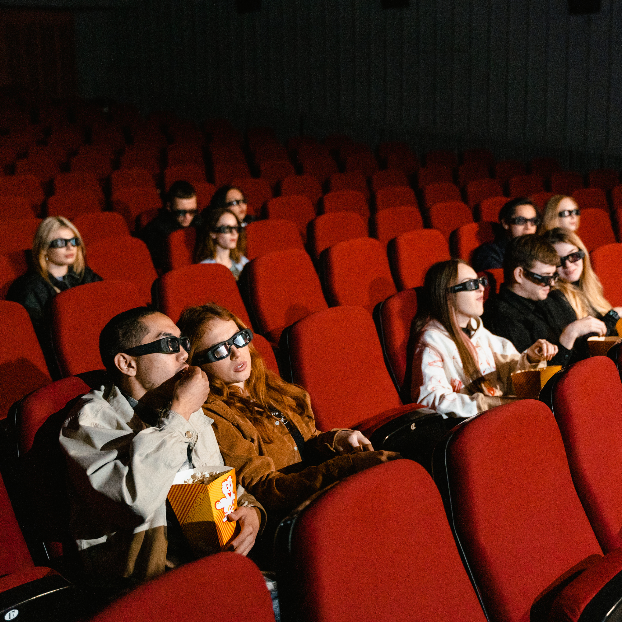 Group of people sitting in theater seats wearing 3D glasses, watching a movie.