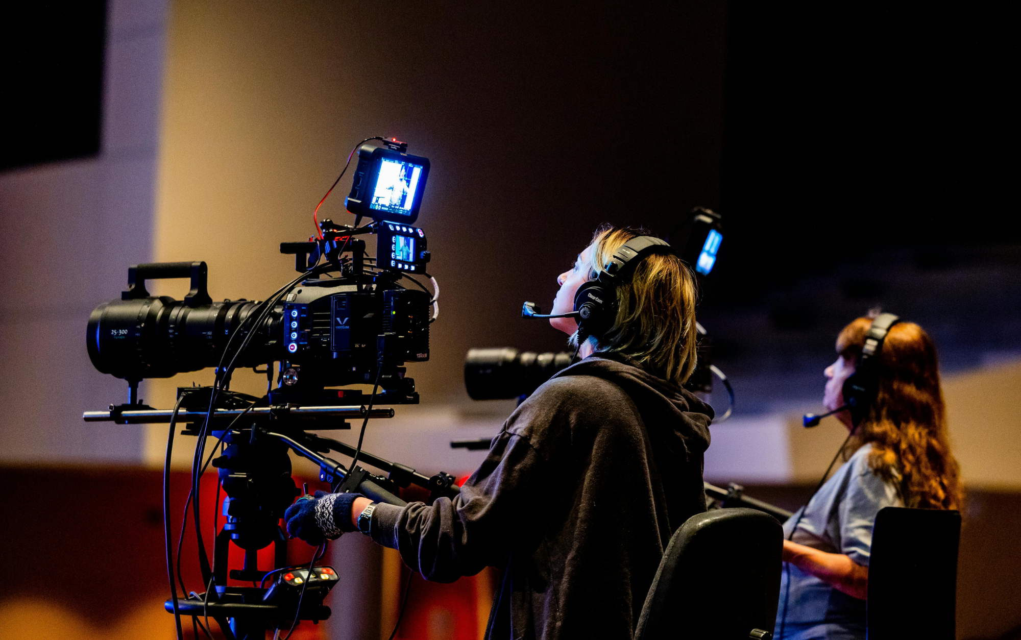 People working with a professional camera setup in a darkened room, possibly a recording studio or TV production environment.