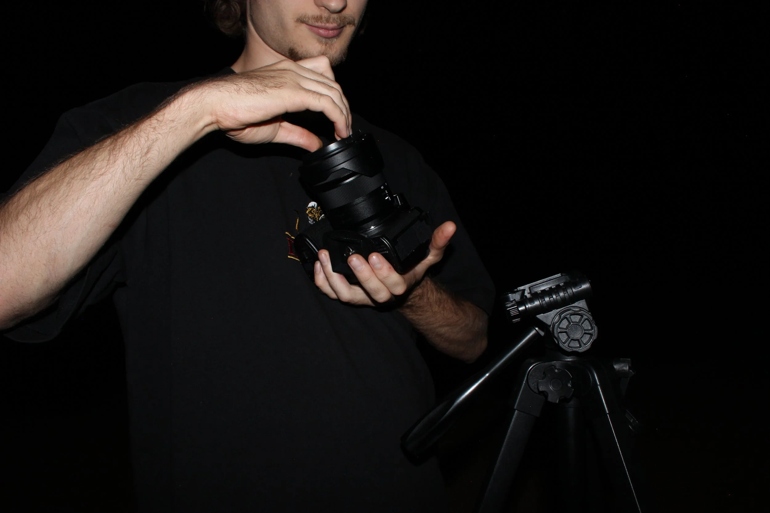 A person holding a camera with a tripod in a dark environment.