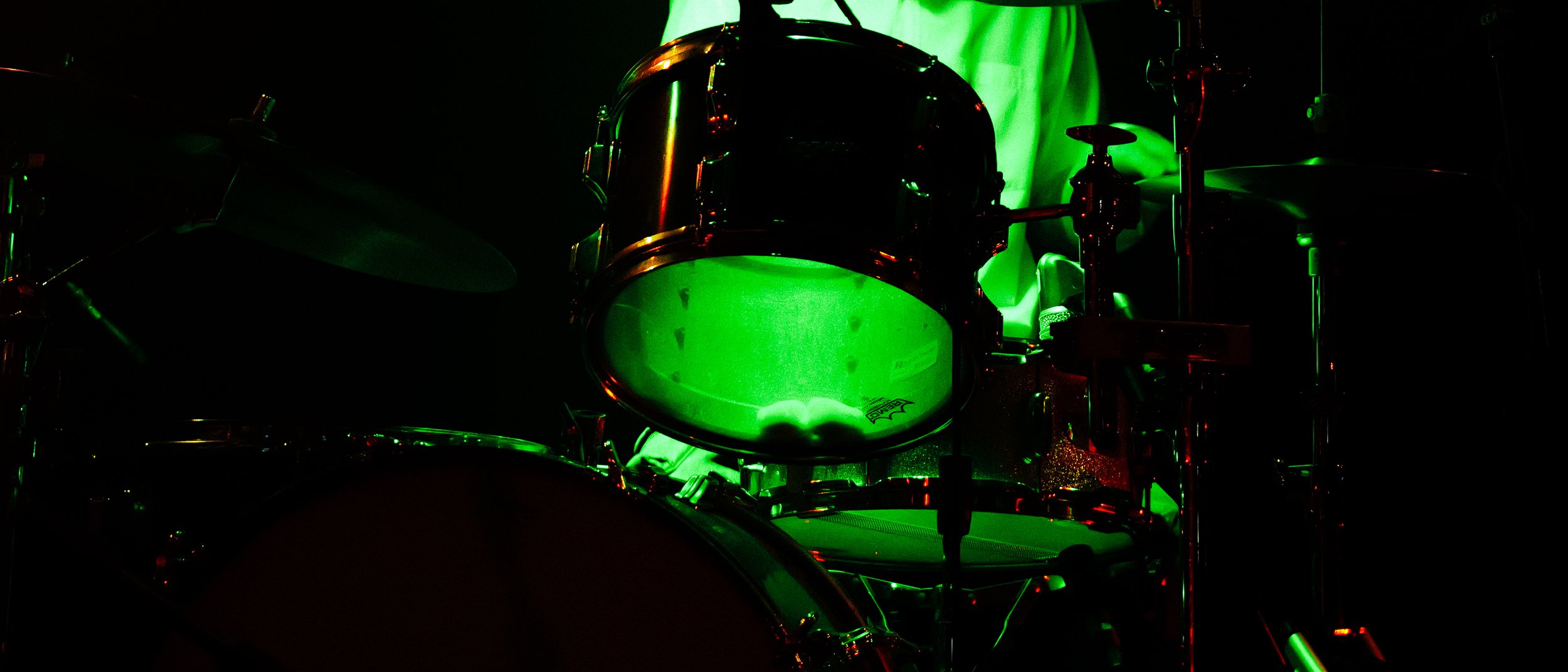 A drum set illuminated with green lighting, featuring drums and cymbals.