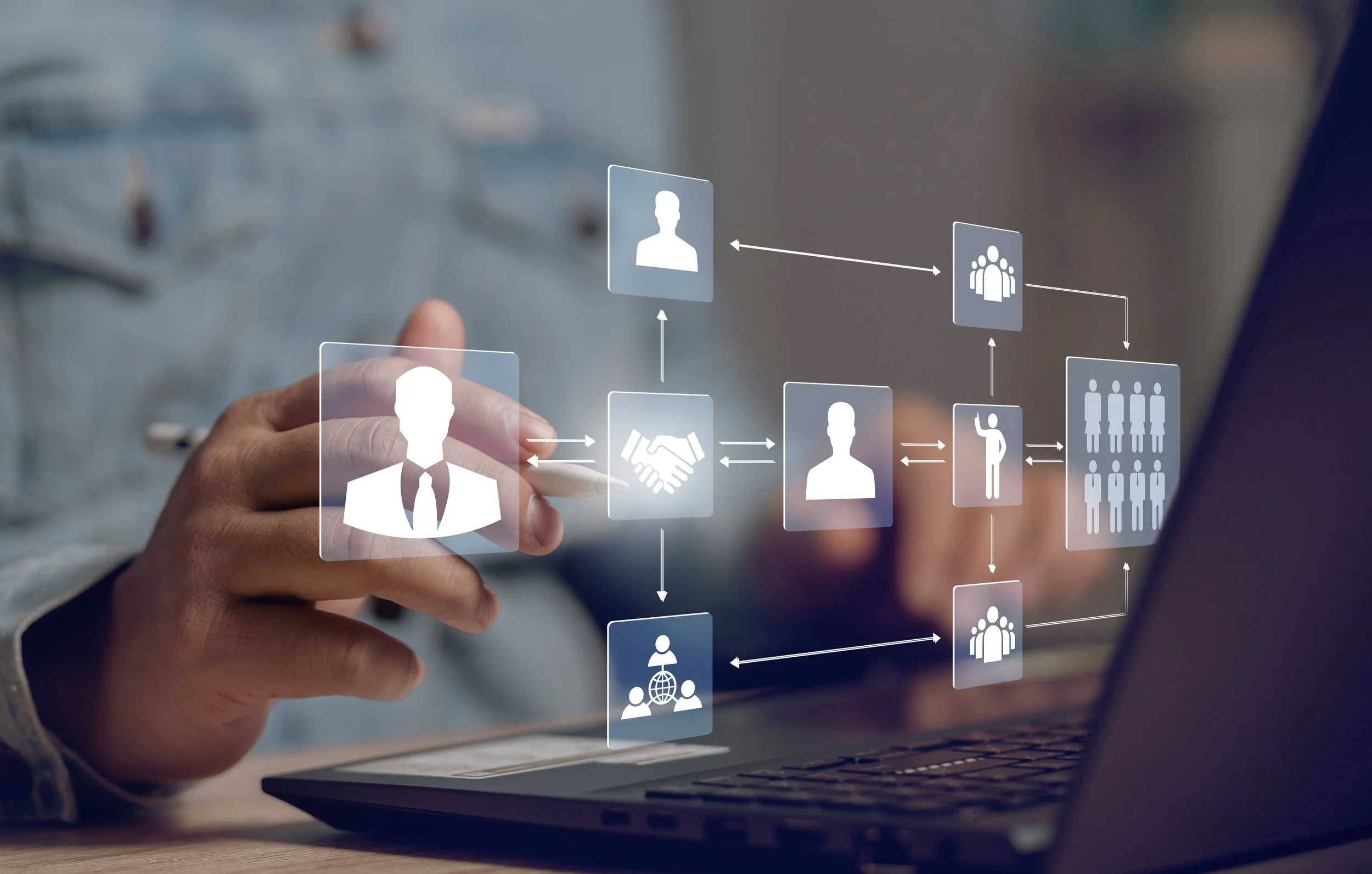 A person in a gray shirt interacts with a holographic digital workflow diagram showing icons of people, a handshake, and connectivity.
