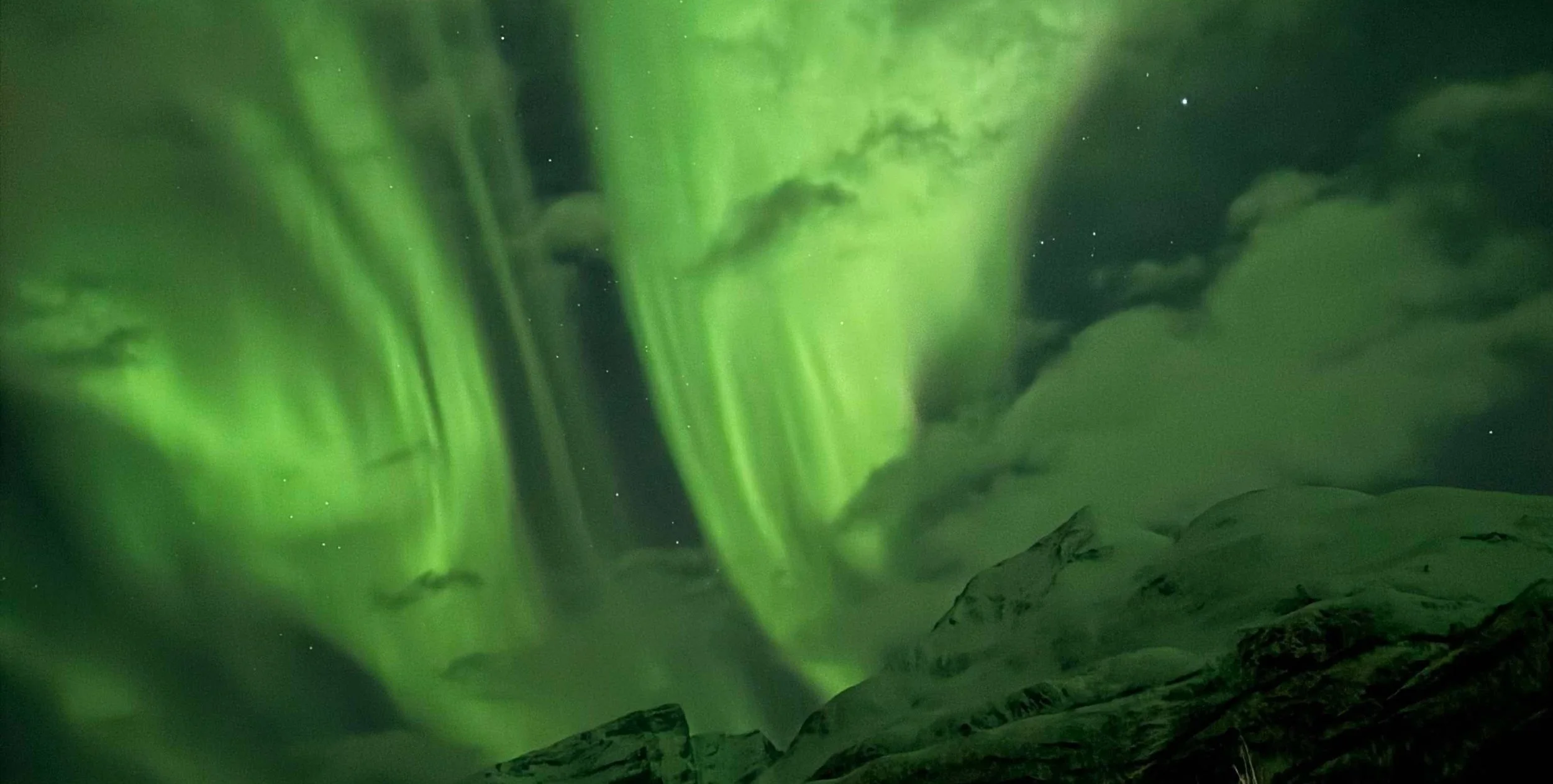 Northern lights (aurora borealis) illuminating the night sky over snow-covered mountains.