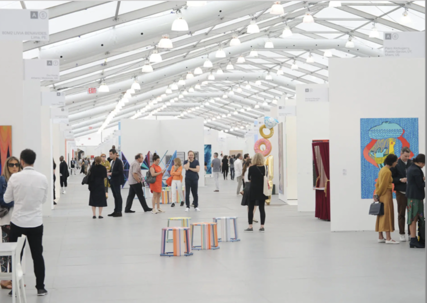 People walking and viewing artwork in an art gallery with white walls and ceiling, and colorful art displays.