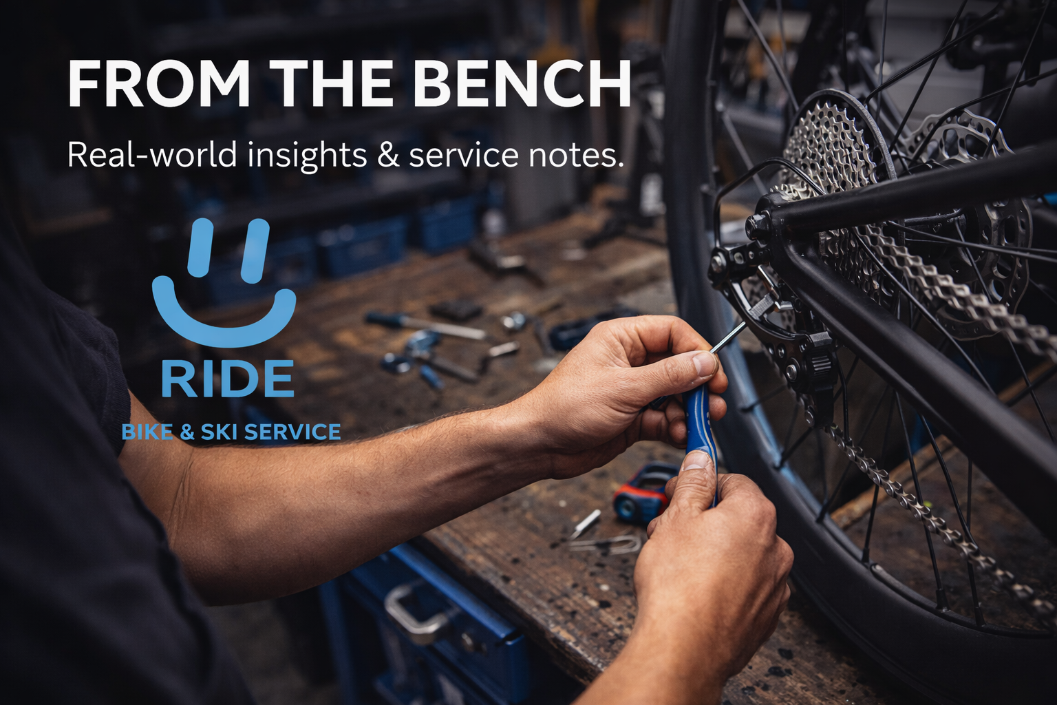 A person repairing a bicycle inside a workshop. The individual is using a screwdriver to work on the bike's gears or chain. The background shows a workbench with various tools and parts, emphasizing a bike and ski service environment.