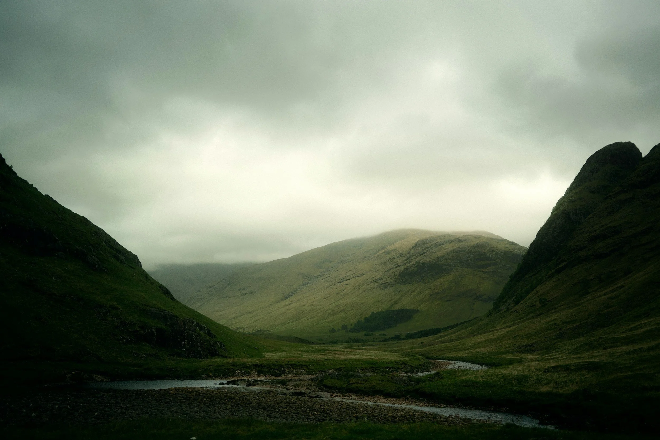 Scenic view of green mountains of the Scottish Highlands with cloudy sky and a river flowing through the glen