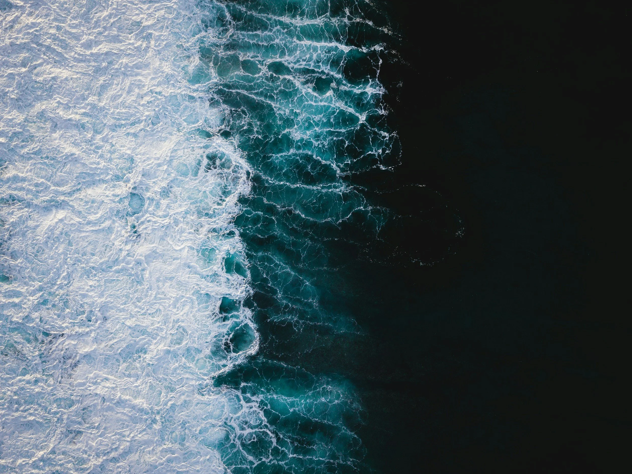 Aerial view of turbulent ocean waves with white foam on a dark blue sea, from the Scottish coastline