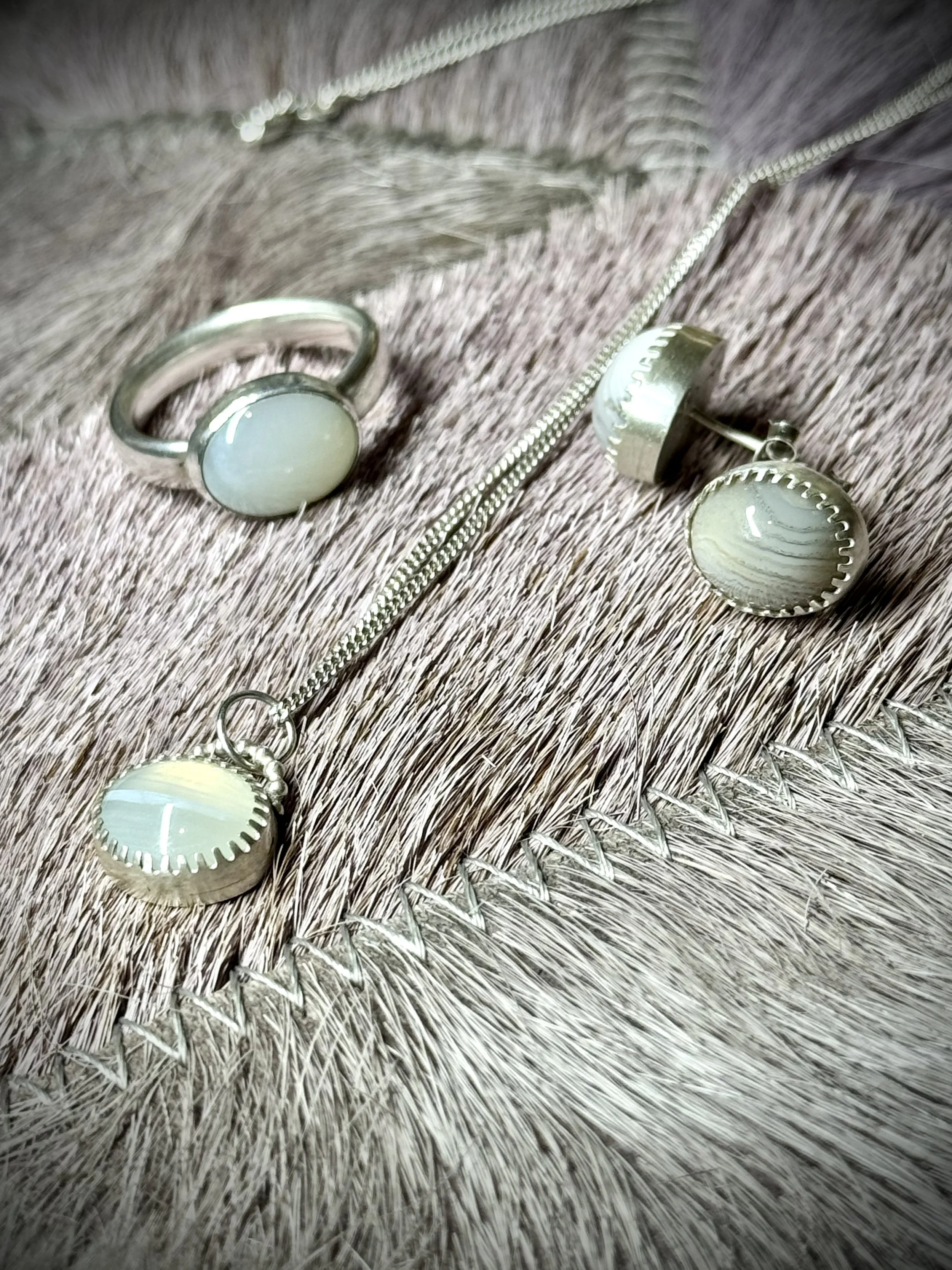 Close-up of silver jewellery items including a ring, a pair of earrings, and a necklace with white stones on a textured fabric surface.