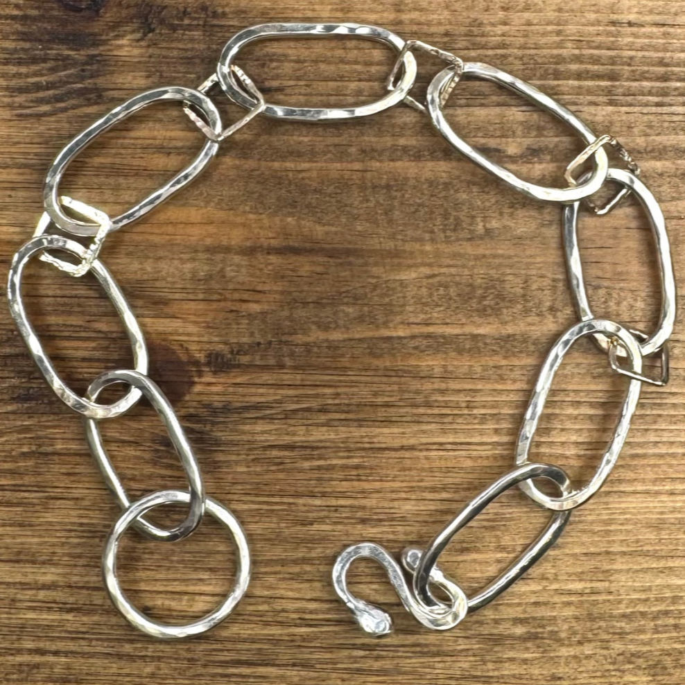 Silver and gold chain-link bracelet on wooden surface.