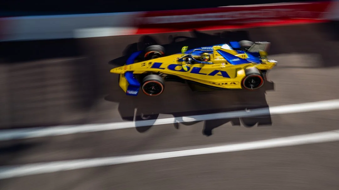 A yellow and blue race car speeding on a racetrack with a blurred background, displaying the word 'POLA' on its side.