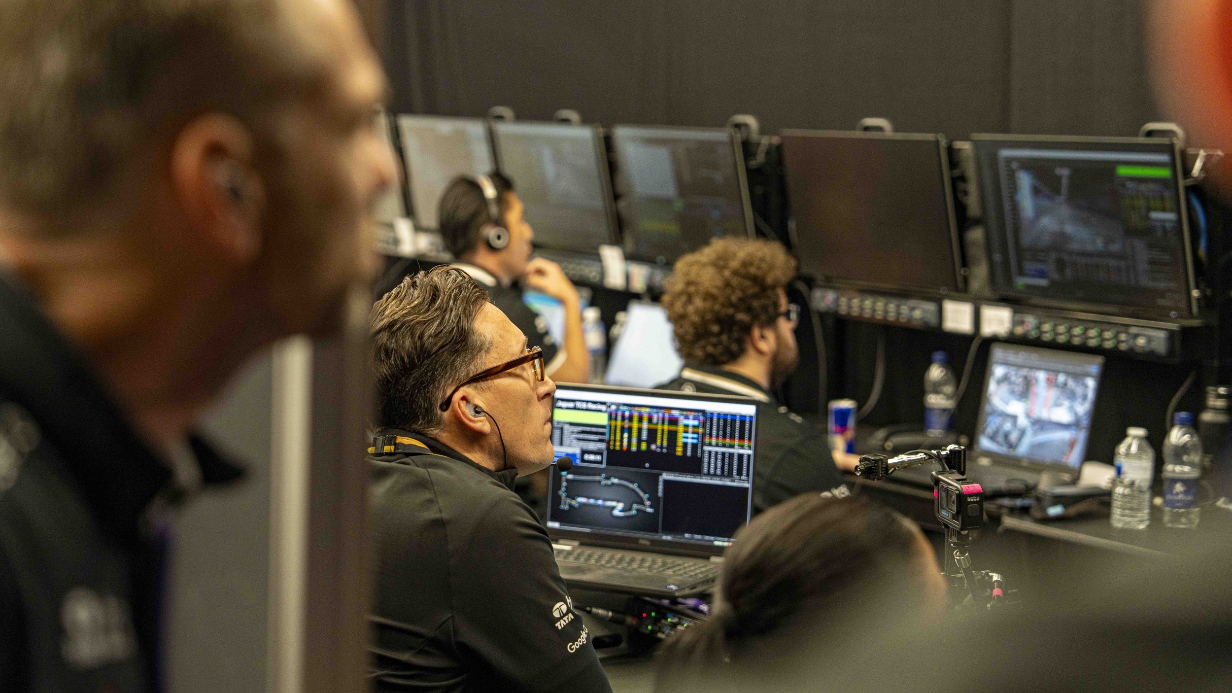 James Barclay, Jaguar TCS Racing Team Principle in the  control room, with multiple monitors displaying racing video feeds and data, several bottles of water on the desk.