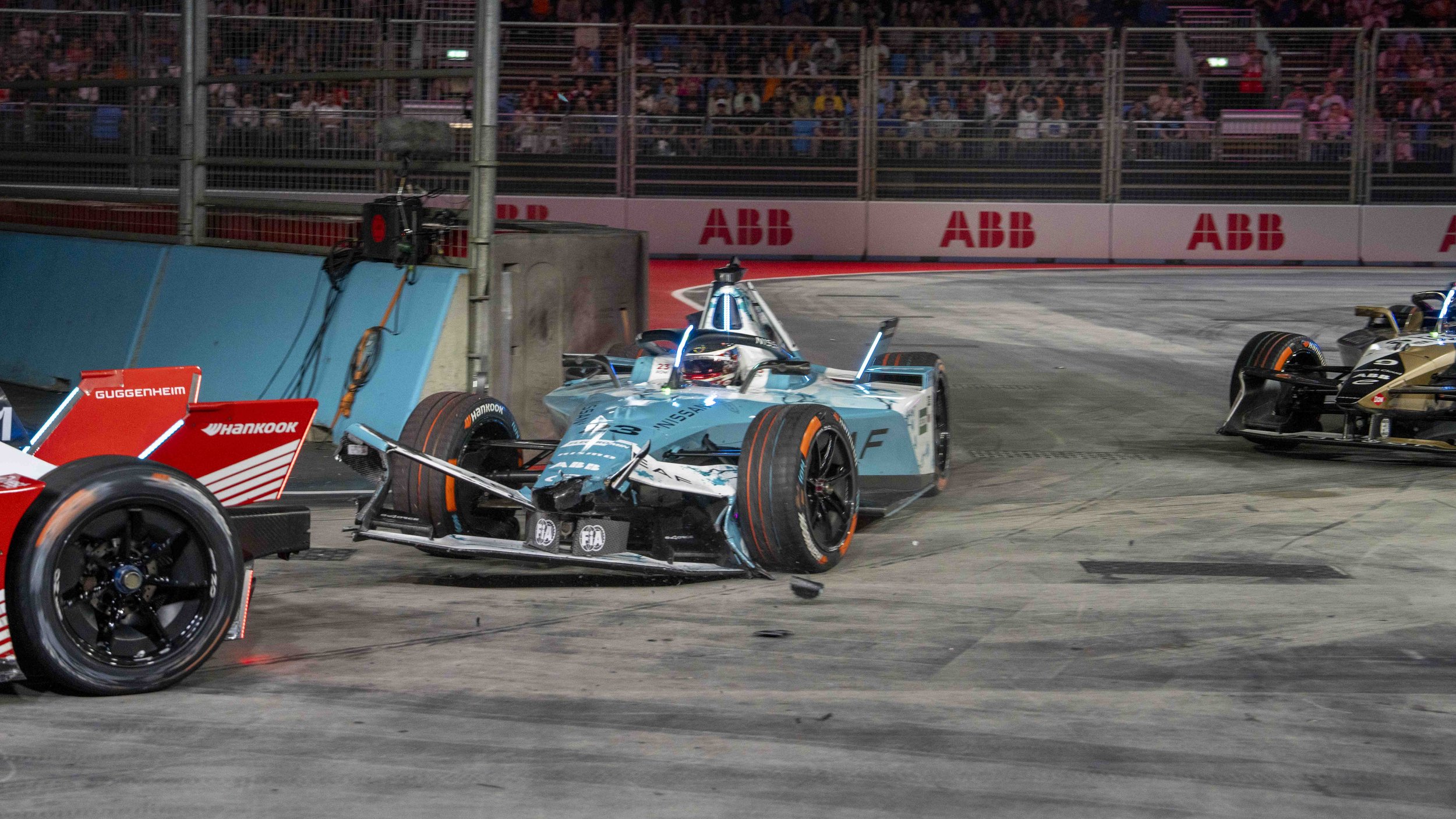 Oliver Rowland, World Champion Formula E driver crashes during the final race, with multiple race cars involved and debris on the track, spectators in the background.
