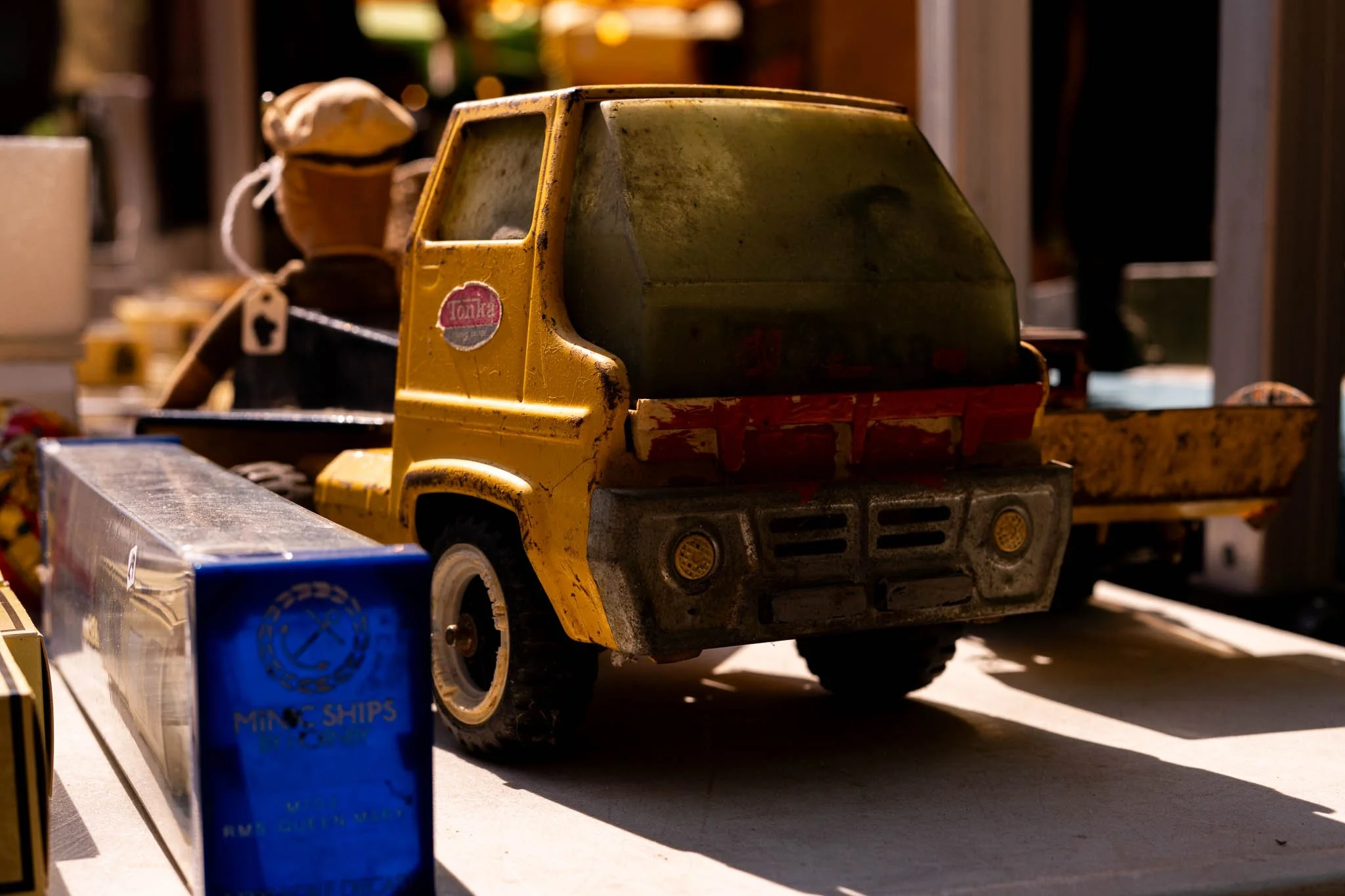 Rusty toy Tonka truck with yellow and black colors on a table, with other toys and objects in the background.