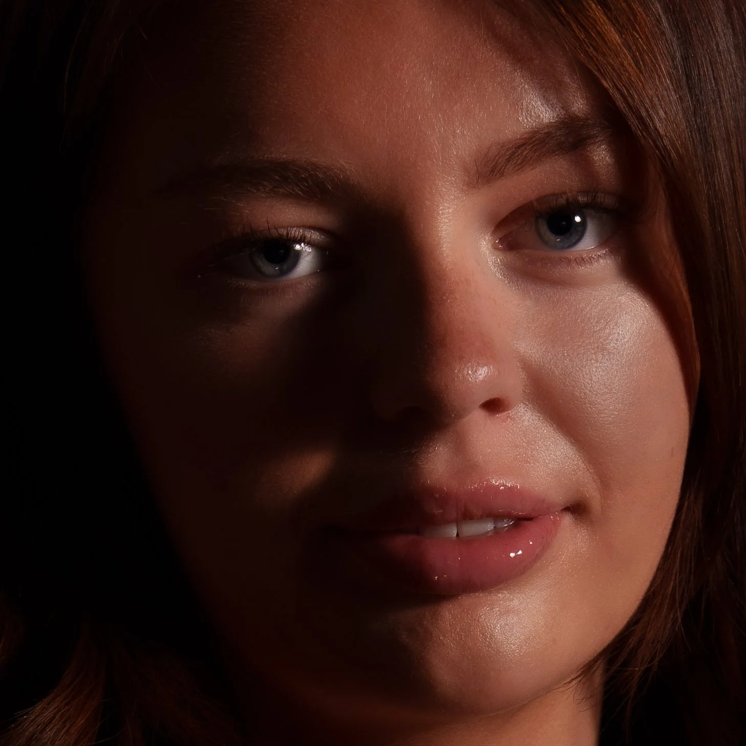 Close-up of a young woman's face with light makeup, highlighting her blue eyes, well-groomed eyebrows, and lips, with a natural complexion and brown hair.
