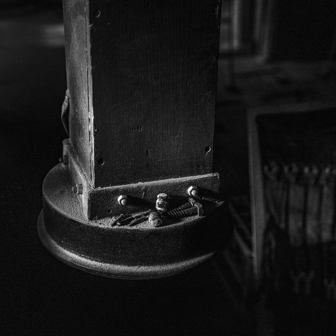 Close-up black and white photo of the base of an old, worn wooden speaker with several screws and parts on the round metal platform, with a blurred background.
