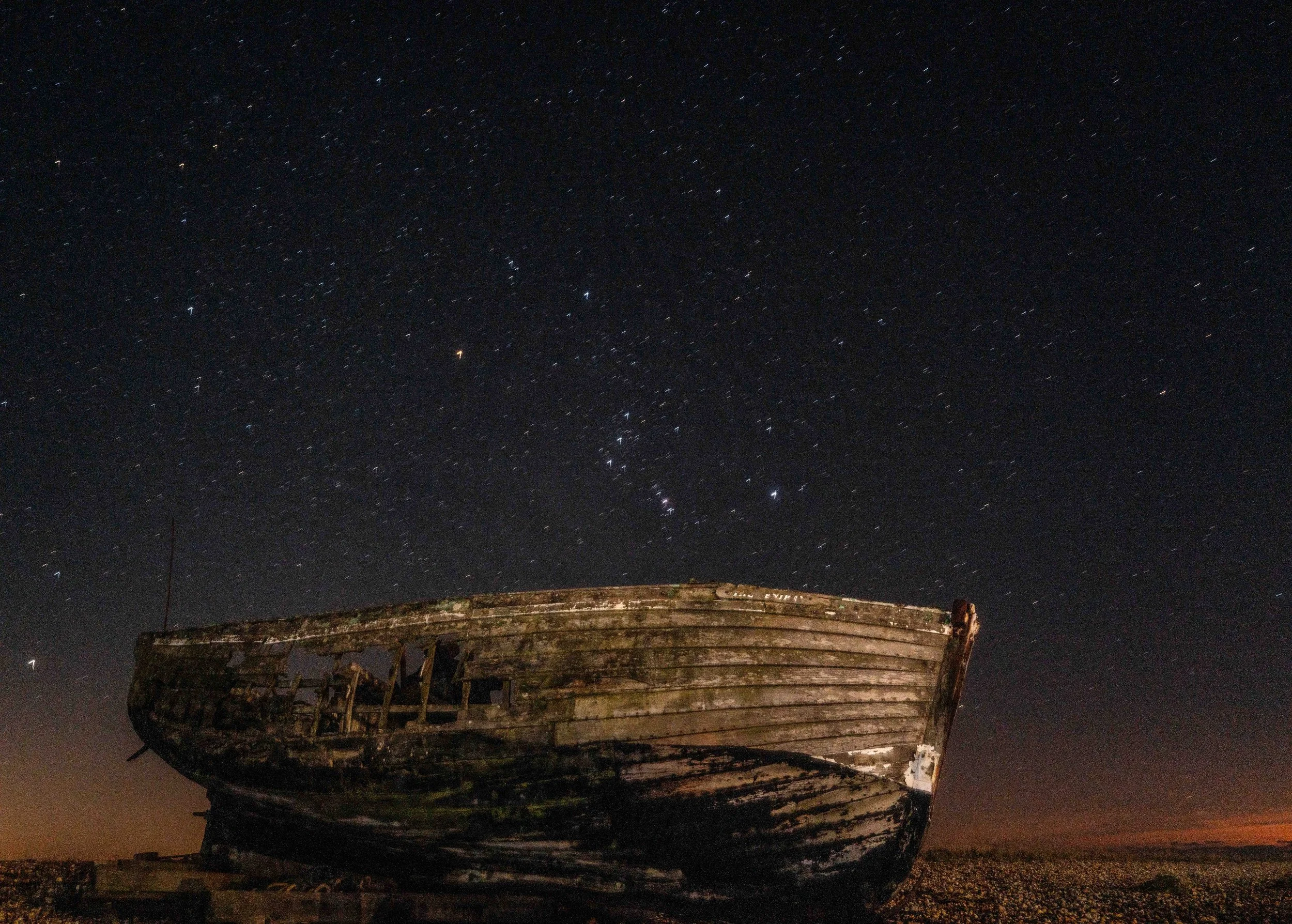 Old, abandoned wooden boat on land beneath a starry night sky in Dungeness