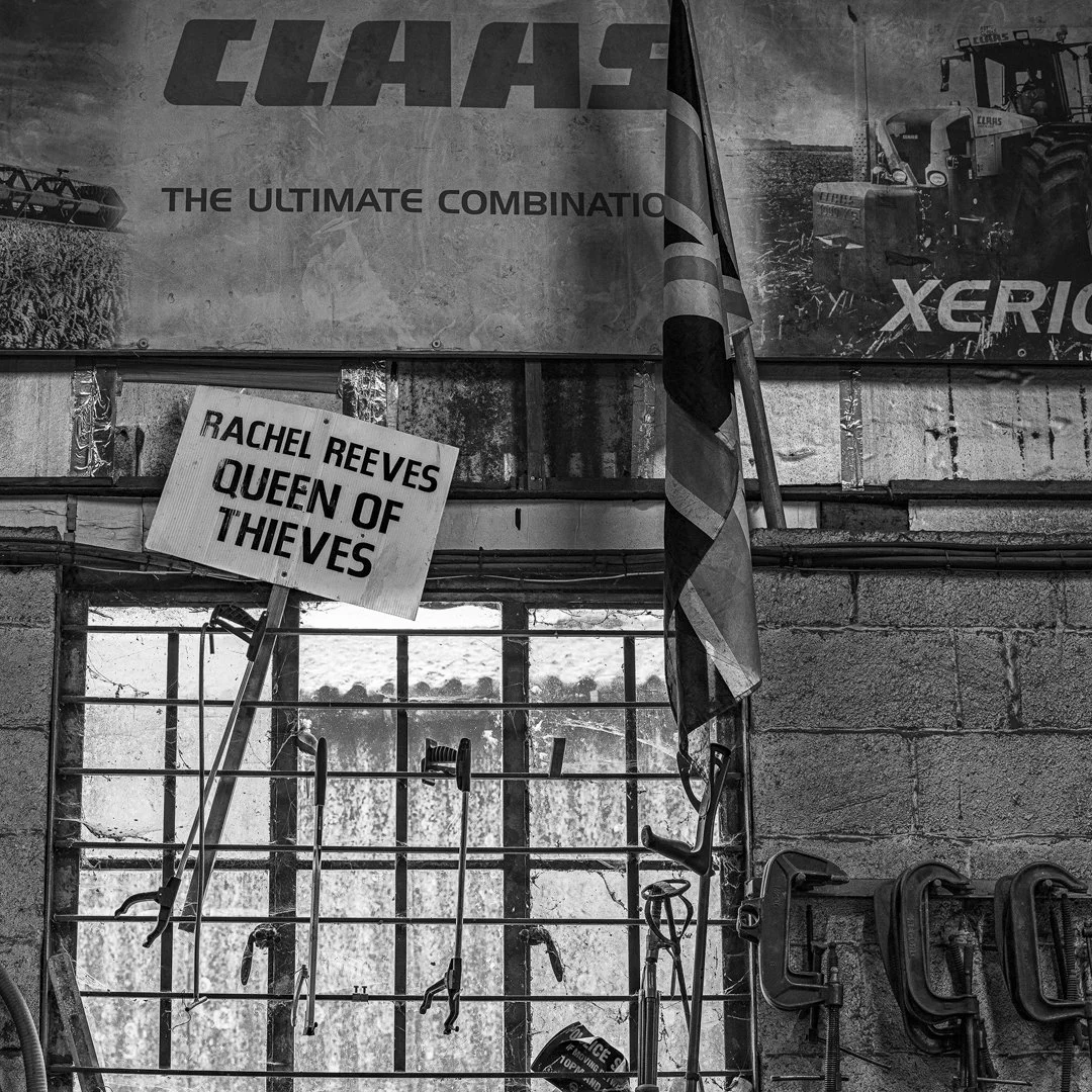 A corner of a workshop with a sign reading 'Rachel Reeves Queen of Thieves', exercise equipment, a window, and posters including one about Claas tractors.