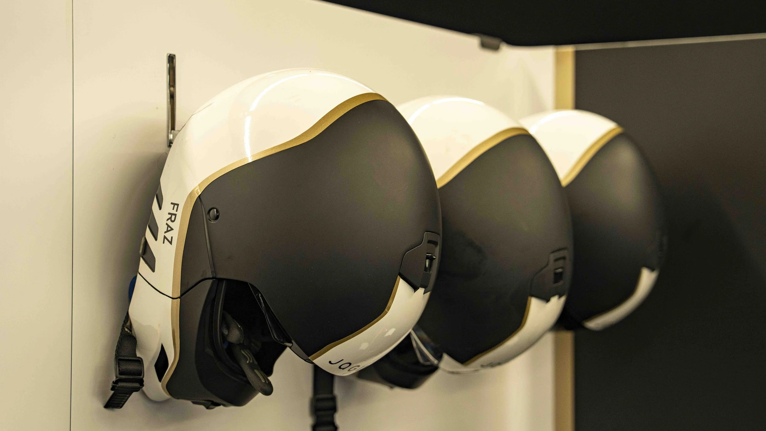 Three black and white mechanics helmets with gold accents hanging on a wall.