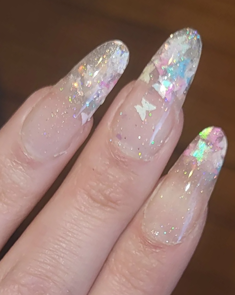 Close-up of four fingers with gel nails decorated with iridescent glitter and holographic foil accents.
