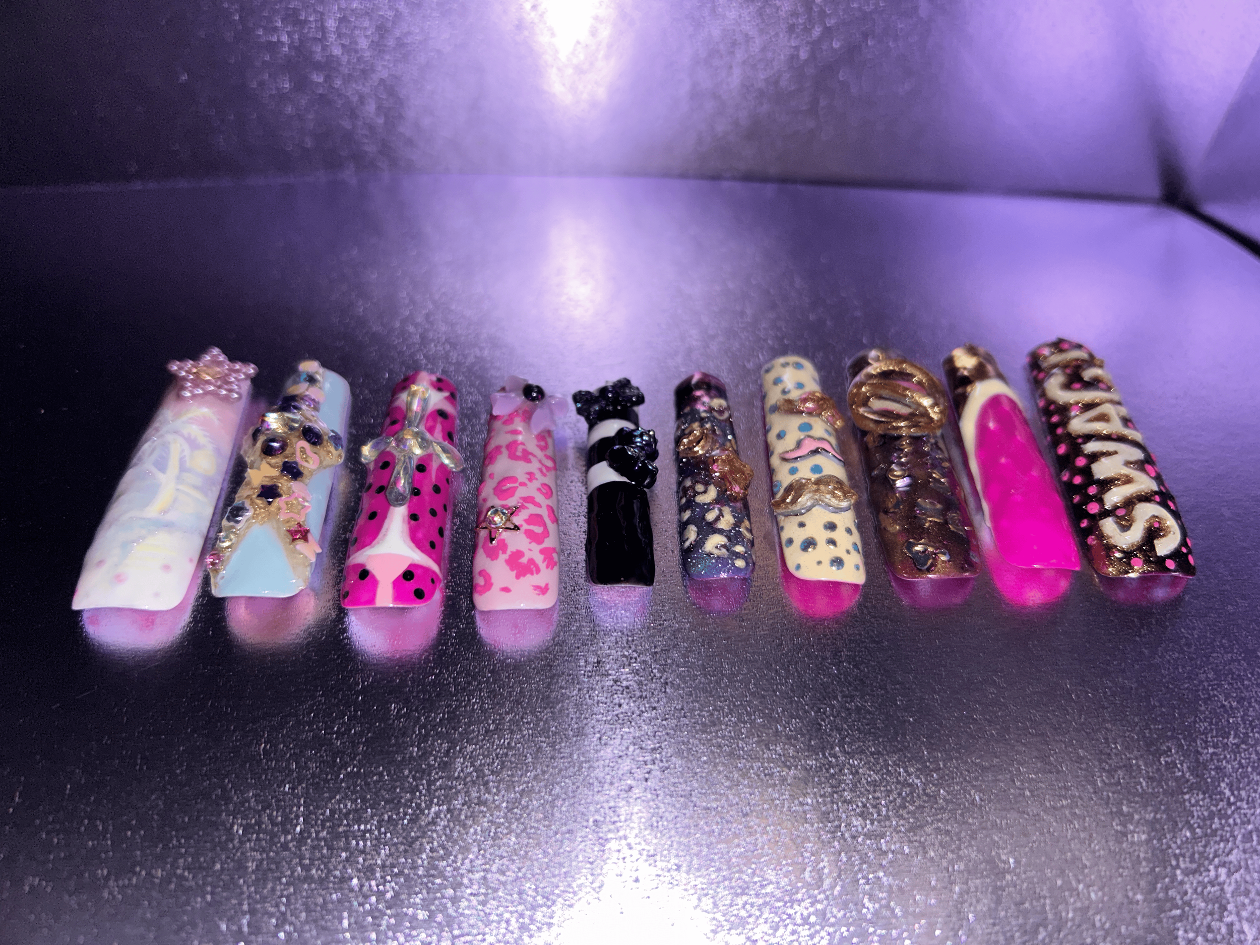 A row of ten decorated hair clips with various colors and patterns, some with embellishments like stars, beads, and gold accents, arranged on a black surface.