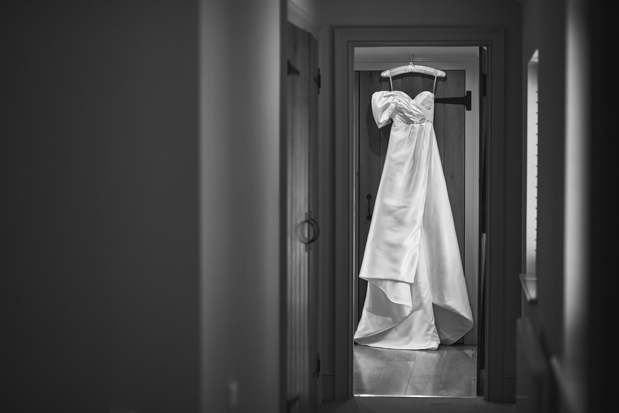 A wedding dress hanging on a door frame in a hallway, with the dress flowing down to the floor.
