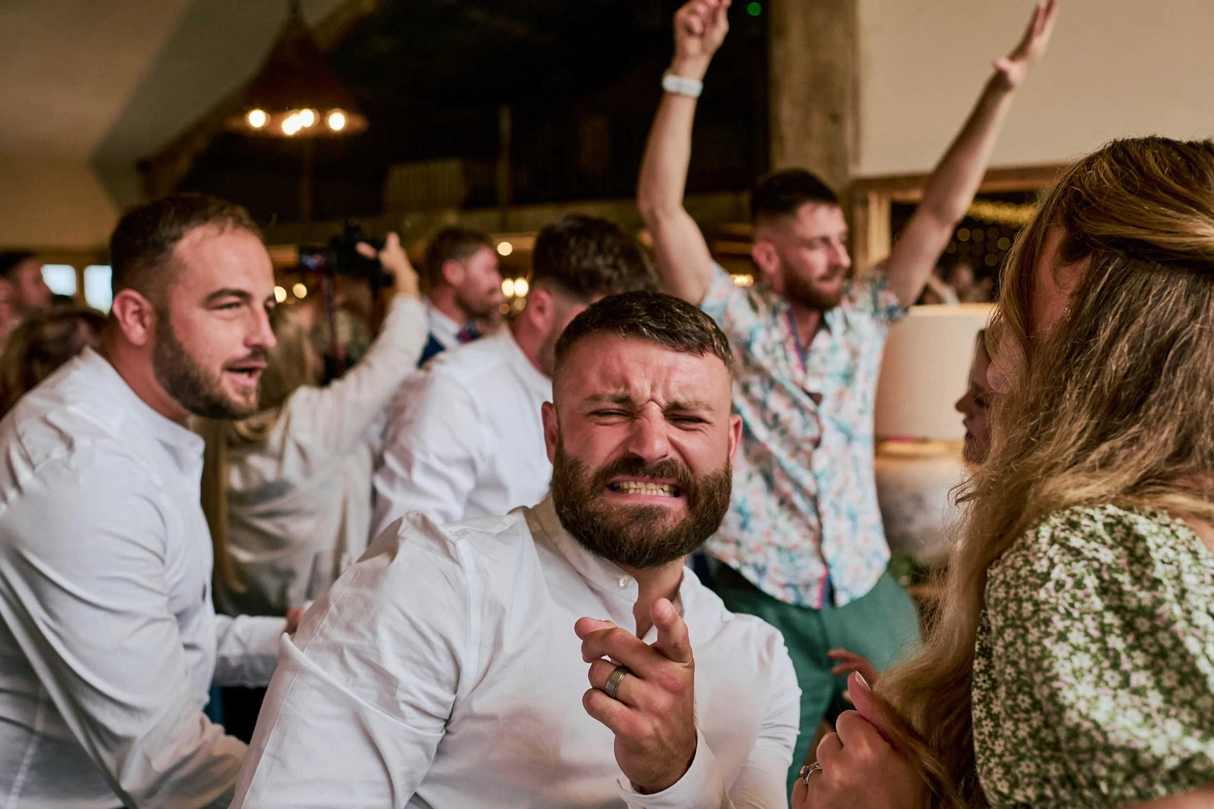 A group of people at a social gathering, with some raising their hands and smiling or making faces, indicating a lively and cheerful atmosphere.