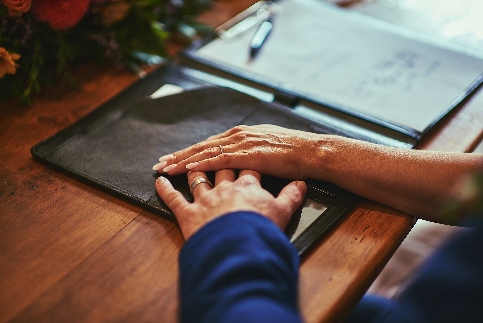 Close-up of a person holding hands on a wooden table with a black folder and a notebook nearby.