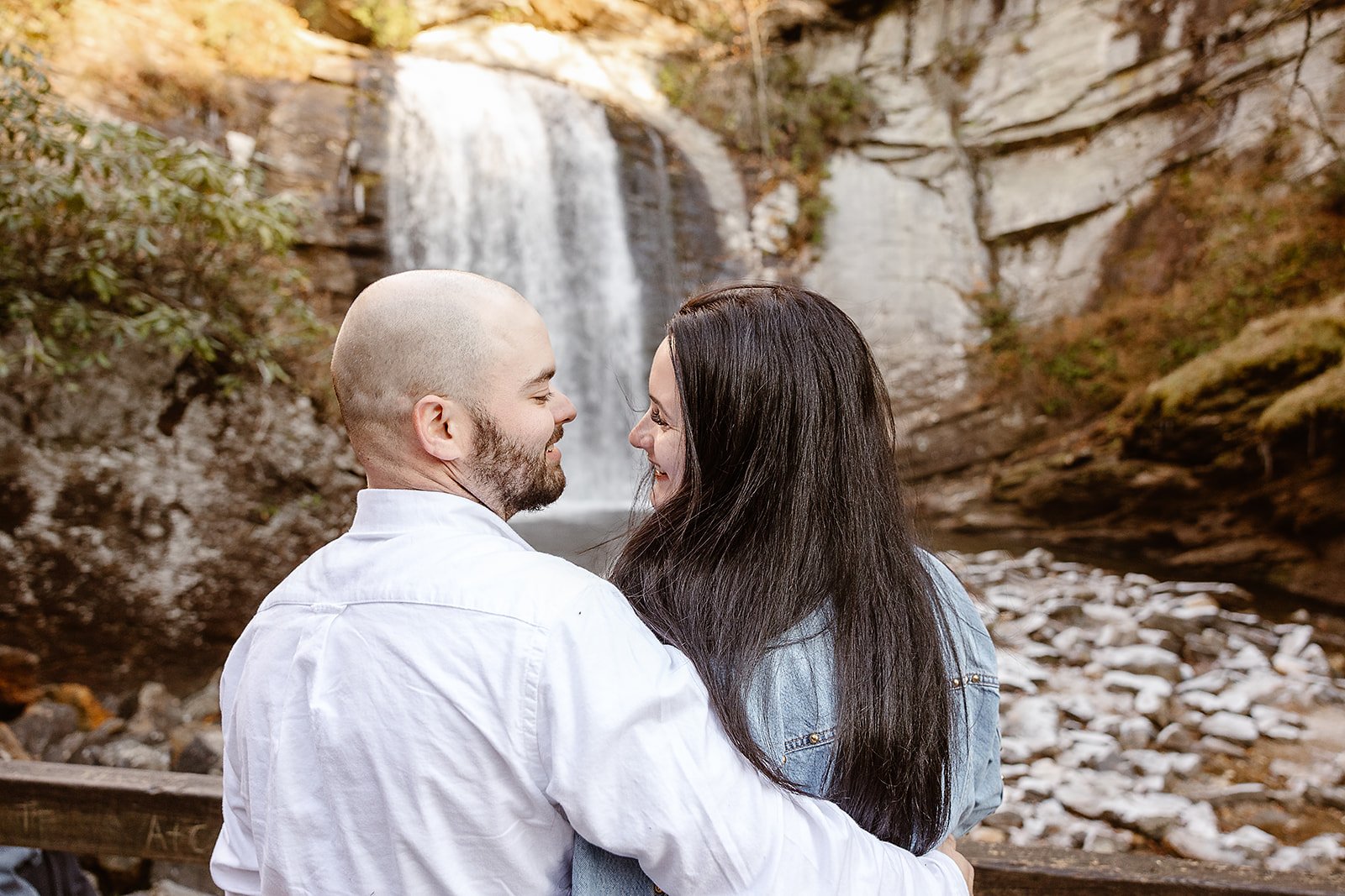 A couple embraces near a waterfall in a natural outdoor setting.