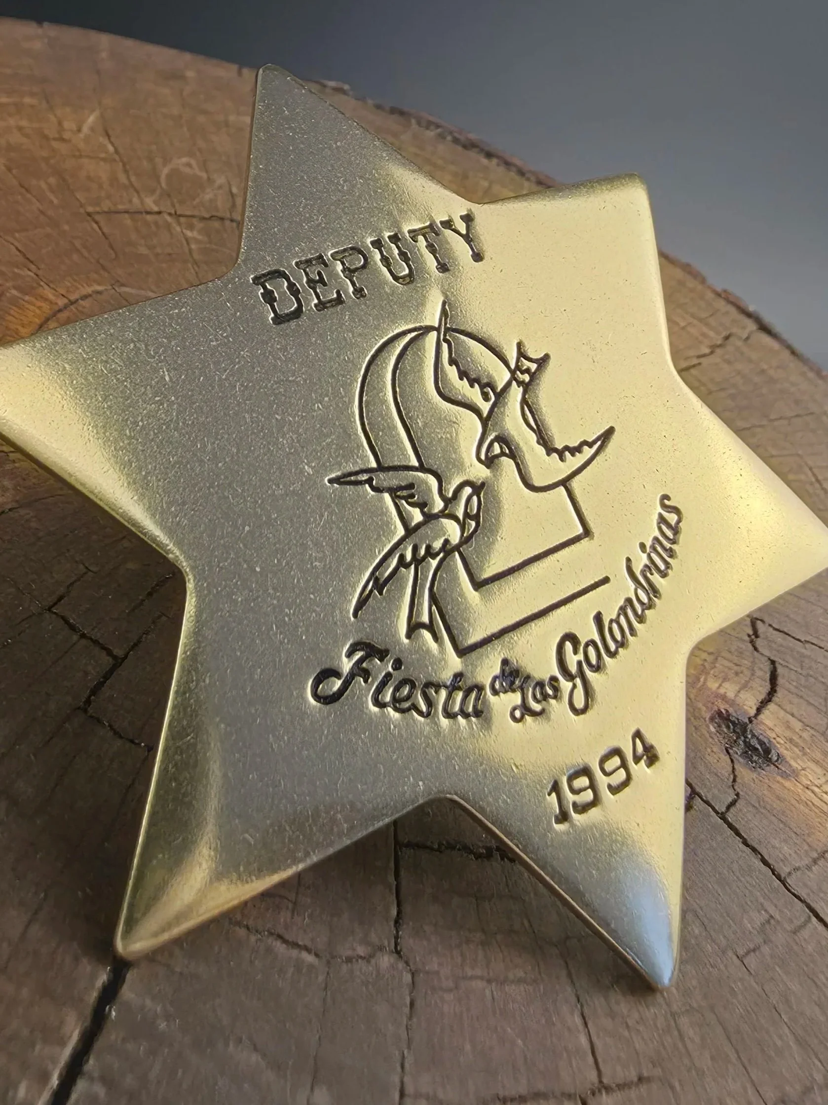 A gold-colored star-shaped badge with engraved text and a graphic of two faces touching foreheads and mussed hair, placed on a wooden surface.