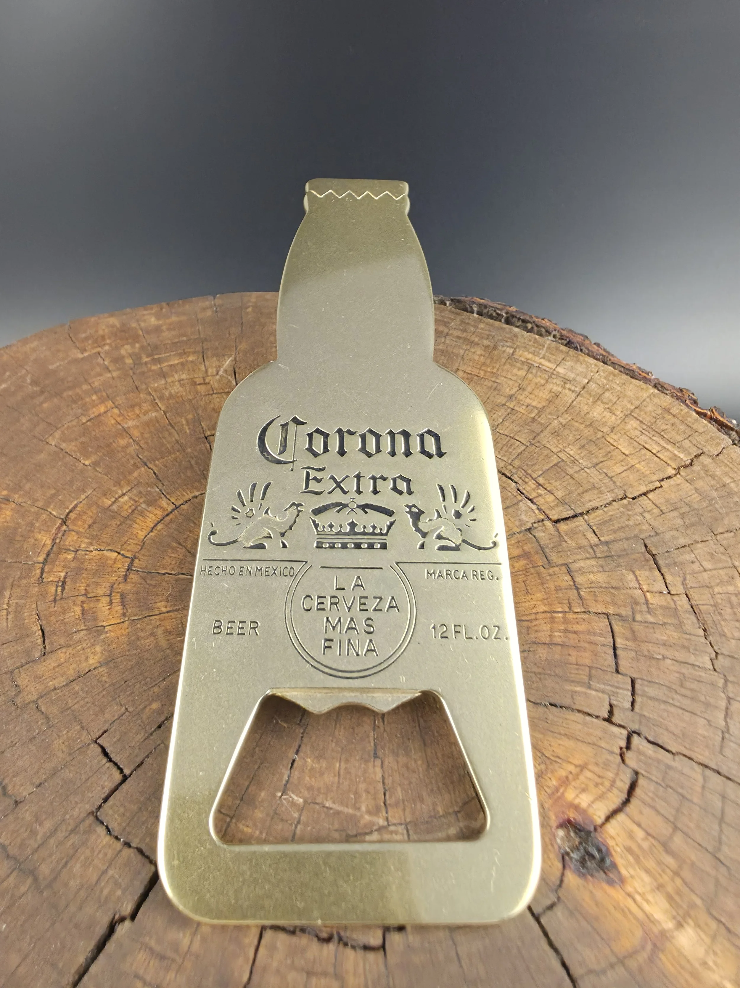 A golden bottle opener shaped like a beer bottle with the 'Corona Extra' logo, placed on a wooden surface.