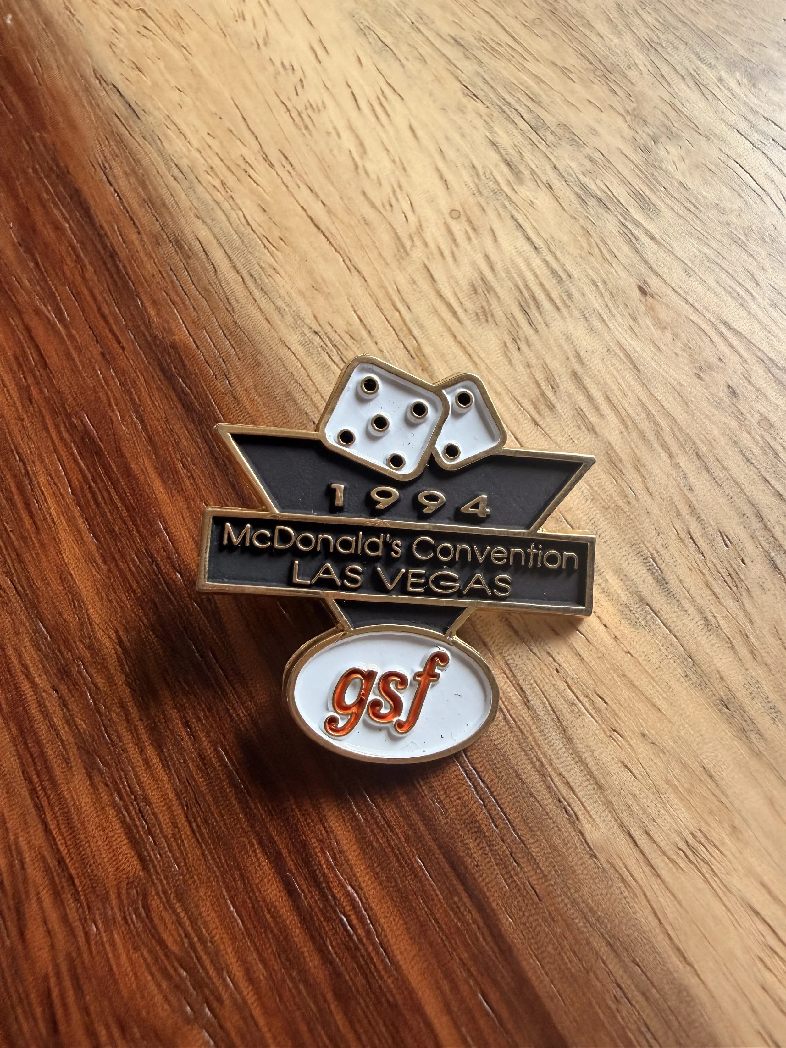 Decorative pins with the McDonald's logo, featuring the year 1994 and the words 'McDonald's Convention LAS VEGAS' and 'gsf', placed on a wooden surface.