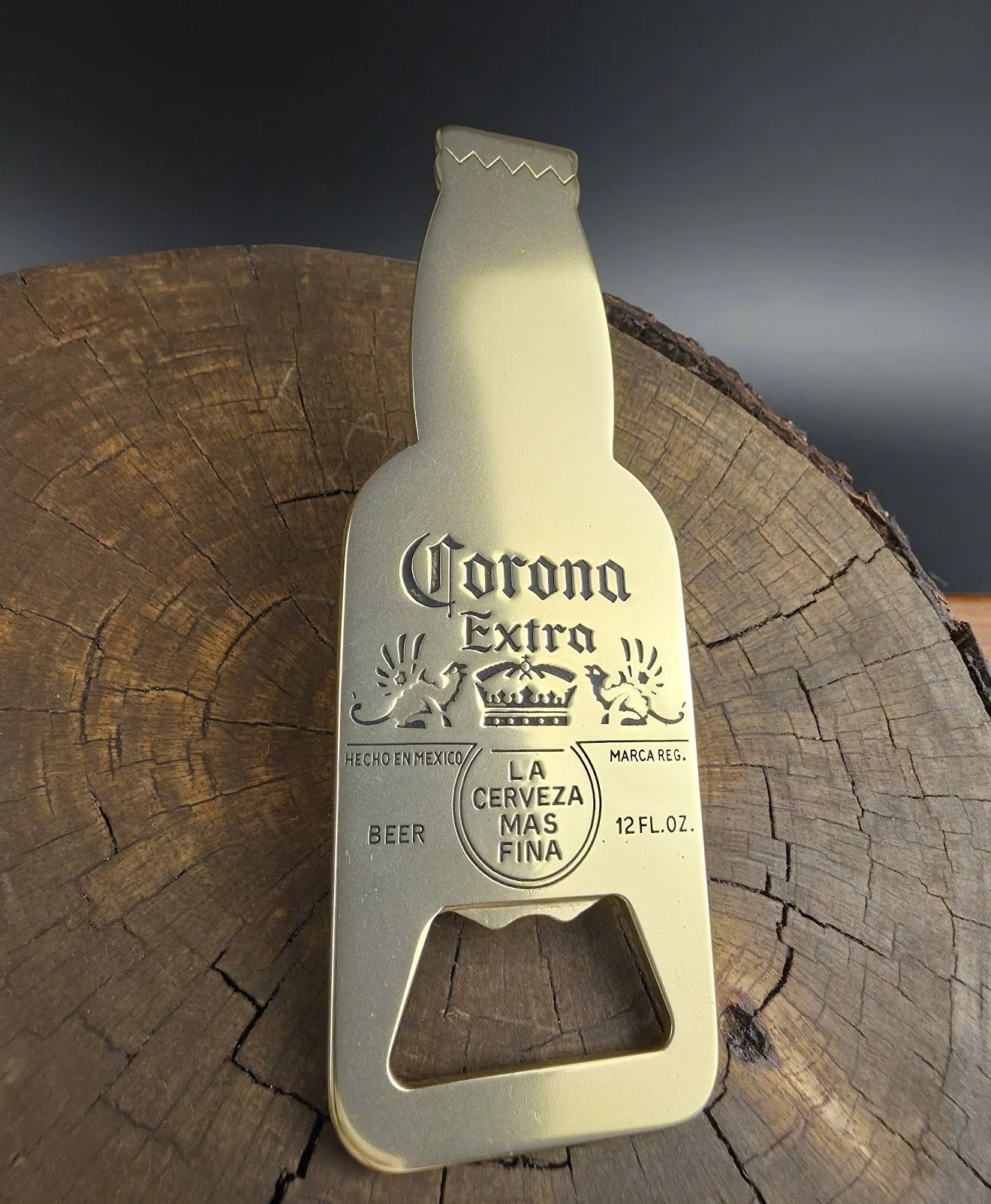 Gold-colored bottle opener with Corona Extra branding, placed on a wooden surface.