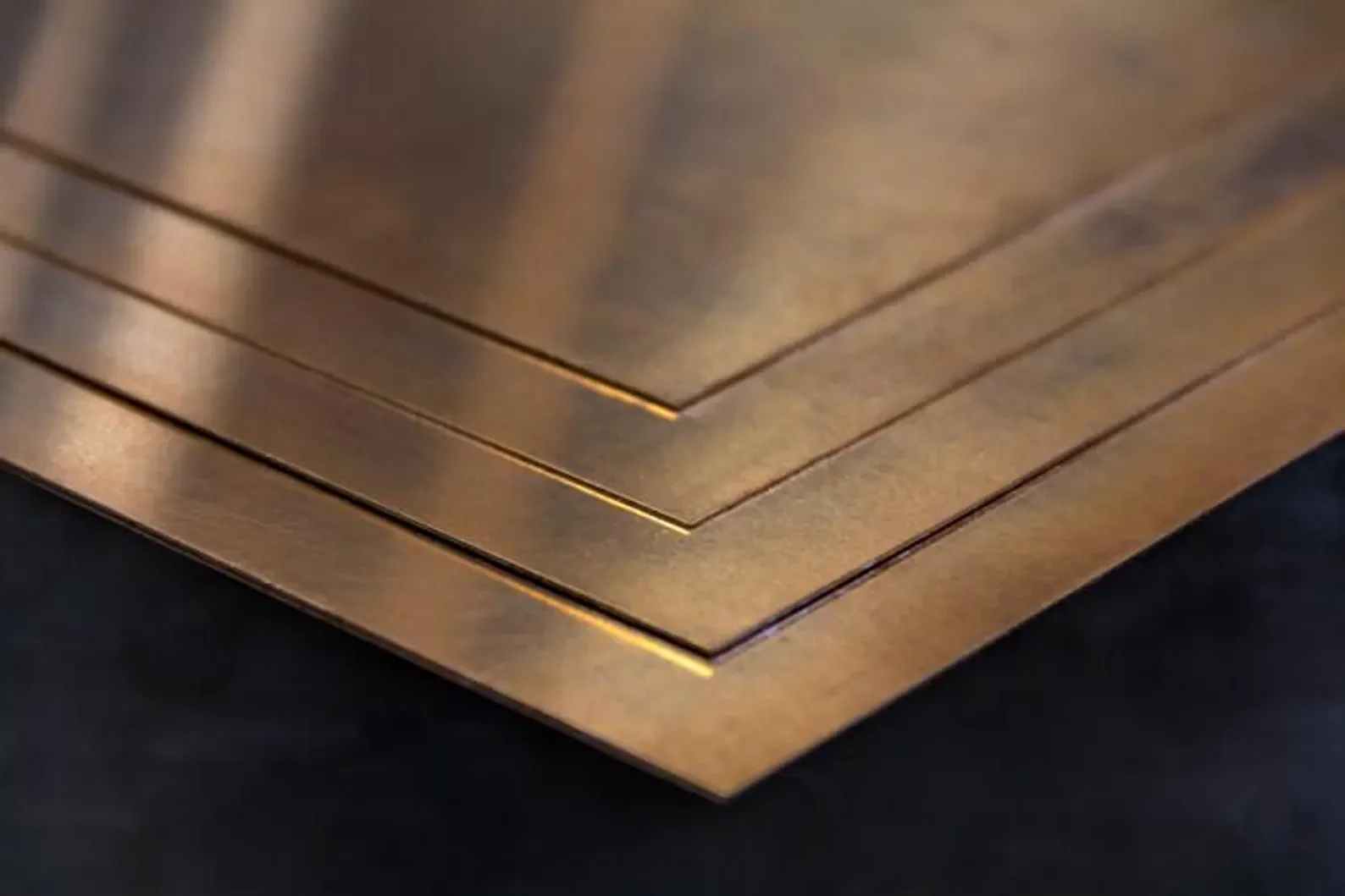 Close-up of stacked bronzed metal sheets on a black surface.