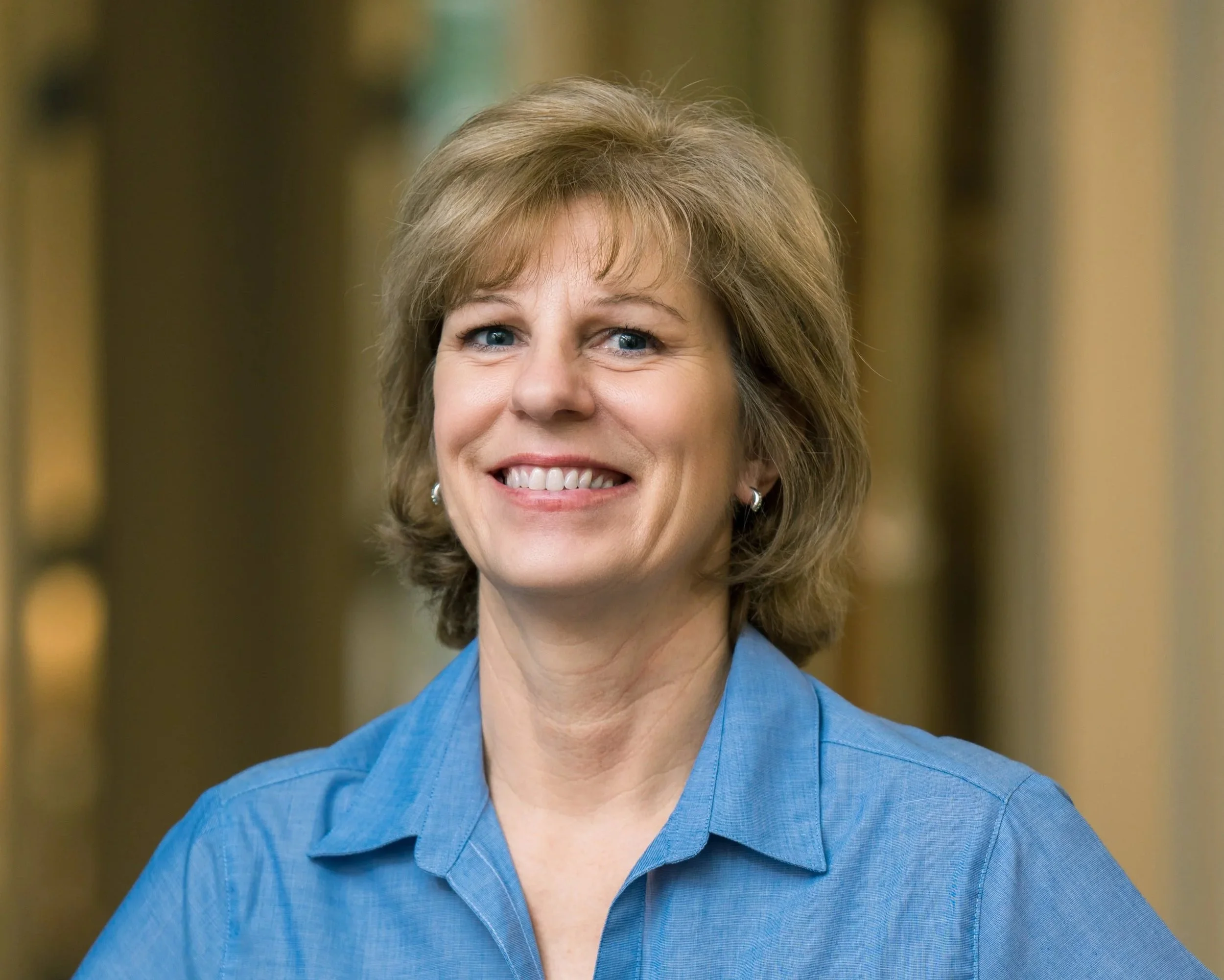 Close-up of a woman with short brown hair wearing a blue collared shirt with the logo 'Spartan Invest' on it.