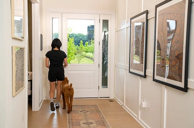 A woman with two dogs standing in a hallway near a glass door leading outside to a green yard.