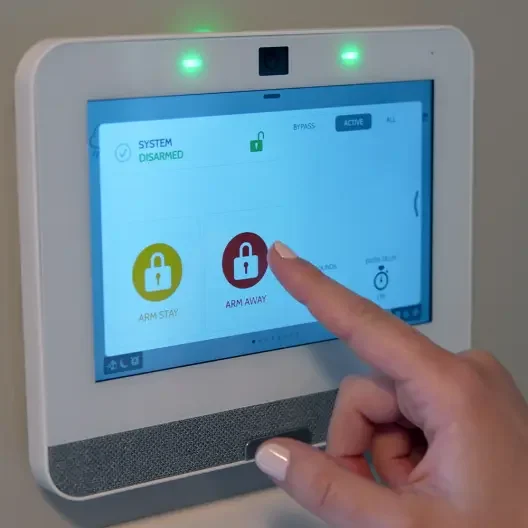 A person using a touchscreen control panel to arm or disarm a security system, with options for 'Arm Stay' and 'Arm Away'.